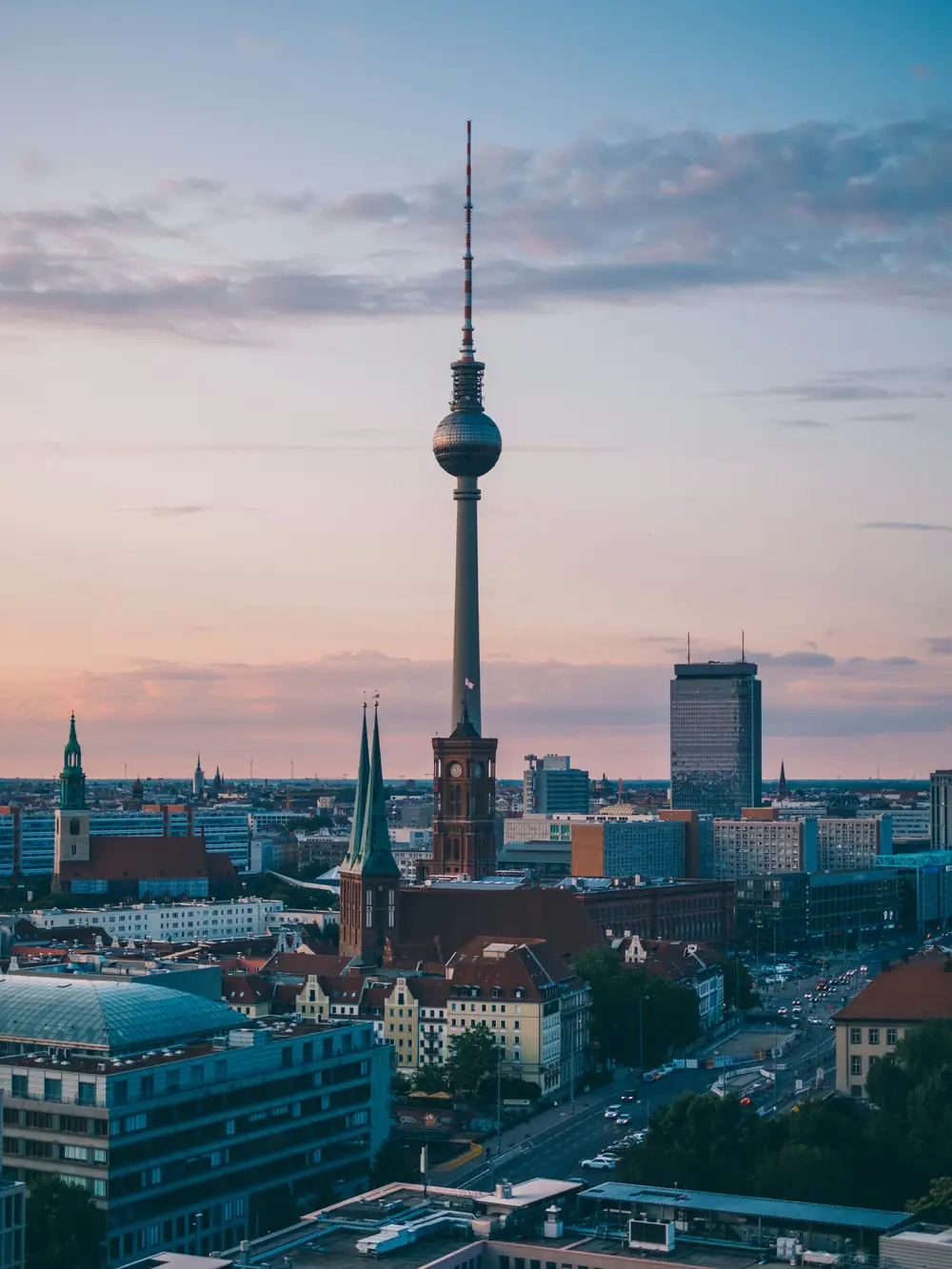 The Berlin television tower above Alexanderplatz at dusk, rooftops running to the horizon.